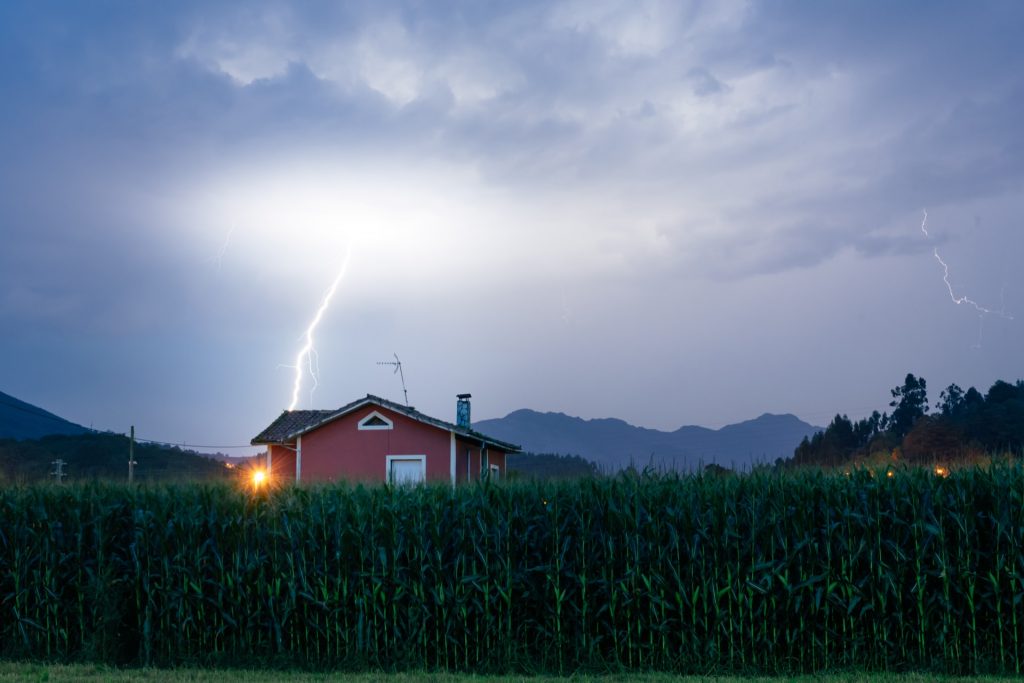 Gewitter mit Blitzschlag ueber einem Landhaus - Blitzschutz und Versicherung fuer Ferienhaeuser