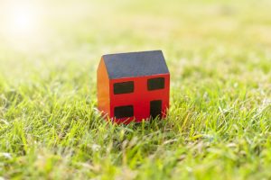 Holzhaus-Modell auf gruenem Rasen - Vergleich Ferienhaus-Versicherung und Wohngebaeudeversicherung